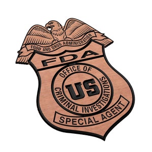 May include: A brown wooden badge with a black border and the text "FDA Office of Criminal Investigations Special Agent" and a black and white image of an eagle with the text "Food and Drug Administration" above the eagle.