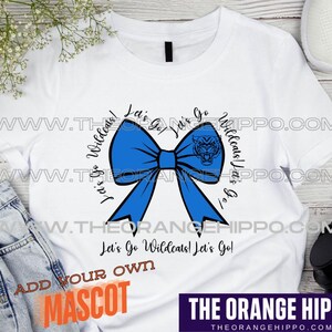 May include: White t-shirt with a blue bow and the text "Let's Go Wildcats! Let's Go!"  The bow has a mascot in the center. The text "Add Your Own Mascot" is at the bottom of the shirt.