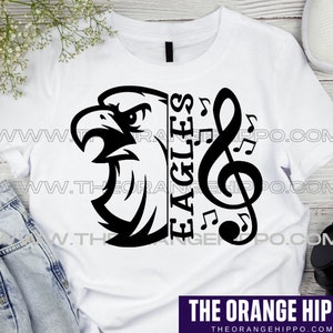 May include: White t-shirt featuring a black graphic of an eagle's head, musical notes, and the word "EAGLES". The design includes a treble clef and musical notes. The text "THE ORANGE HIPPO" is at the bottom.