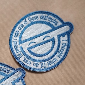 May include: Two embroidered patches with a blue and white design. Each patch features a circular emblem with the text "I thought what I'd do was pretend I was one of those deaf-mutes". The patches have a smiling face.