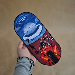 May include: A red and blue embroidered patch shaped like a pill. One side features a blue and white image of a spaceship. The other side features a red and yellow image of a motorcycle and a person riding it. The text "FFFF" is visible on the red side.