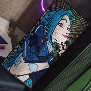 May include: Embroidered patch featuring a character with blue hair and red eyes, set against a black and gold textured background. The character is depicted with a thoughtful expression, wearing blue attire. The patch is rectangular.