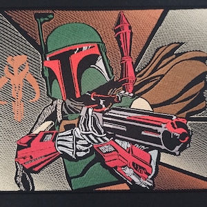 Pode incluir: Patch bordado com Boba Fett de Star Wars. O patch mostra o personagem em sua armadura verde e vermelha, segurando um blaster. O fundo apresenta formas geométricas em marrom, bege e cinza.