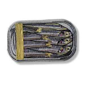 May include: Embroidered patch depicting a sardine can. The can is gray with a gold pull tab. Inside, several sardines are visible, with detailed stitching in shades of gray, brown, and yellow. The patch is rectangular with rounded corners.