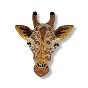 May include: An embroidered giraffe head patch featuring a detailed brown and tan spotted pattern. The design includes two small ossicones with black tips, pointed ears with yellow inner edges, and a stitched snout with black nostril details.