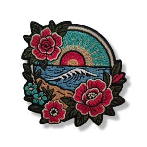 Puede incluir: Un parche bordado que muestra una escena circular de playa con una ola rompiendo, un sol naciente y un cielo turquesa. El diseño está enmarcado por flores rosas y rojas vibrantes con hojas verdes, todo delineado con un borde negro grueso.