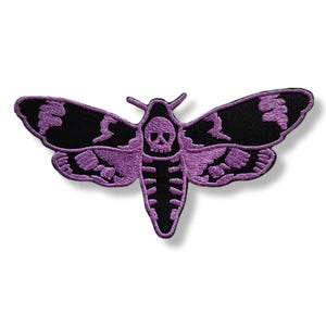 Peut inclure: Écusson brodé représentant un sphinx à tête de mort. Le papillon de nuit a des ailes noires avec des accents violets et un corps violet. La tête du papillon est un crâne. L'écusson est probablement destiné aux vêtements ou aux accessoires.