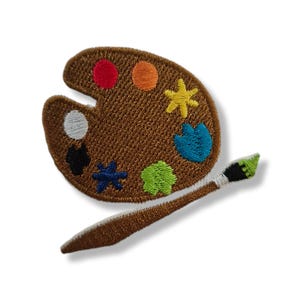 Puede incluir: Un parche bordado que presenta una paleta de artista marrón con manchas de pintura coloridas en rojo, naranja, amarillo, azul, verde, negro y blanco, acompañado de un pincel marrón con punta verde y virola blanca, todo con acabado texturizado.
