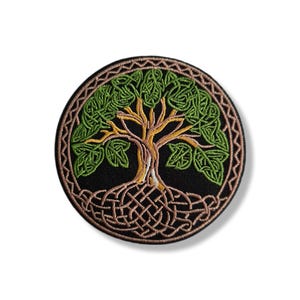 Op de afbeelding: Ronde geborduurde patch met een Keltische levensboom ontwerp. De patch heeft een zwarte achtergrond met een bruine rand. De boom heeft groene bladeren, een gele stam en bruine wortels.