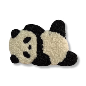 May include: A black and white panda bear rug in a lying down pose. The panda has black ears, eyes, and limbs, and a white body. The rug is made of a soft, textured material, and is designed to look like a panda.