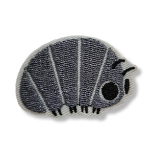 Pode incluir: Um emblema bordado em forma de tatu-bolinha, apresentando um corpo cinza segmentado com uma borda branca. O design inclui um grande olho circular preto, duas pequenas antenas pretas e várias pequenas pernas pretas na borda inferior.