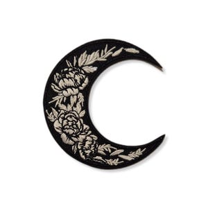 Peut inclure: Patch brodé en forme de croissant de lune noir avec des détails floraux blancs. Le patch présente une forme de croissant de lune stylisée avec un motif floral en fil blanc.