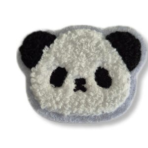 Peut inclure: Un visage de panda blanc et duveteux avec des oreilles et des yeux noirs. Le panda est brodé sur un tissu bleu clair.