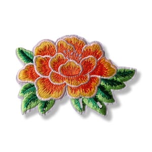Peut inclure: Écusson floral brodé représentant une fleur orange et jaune avec des feuilles vertes. Les pétales de la fleur présentent des coutures détaillées, et les feuilles ont un aspect texturé. L'écusson est probablement destiné à des fins décoratives.