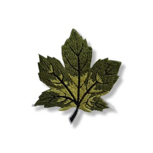 Op de afbeelding: Geborduurde groene esdoornbladpatch met gedetailleerde stiksels. Het blad heeft verschillende tinten groen en geel, met zwarte aderen. Deze decoratieve patch is ideaal om kleding of accessoires een vleugje natuur te geven.