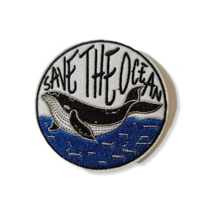 Könnte beinhalten: Ein runder weißer Patch mit blauer und schwarzer Stickerei. Der Patch zeigt einen Wal, der im Meer schwimmt, mit dem Text "Save The Ocean" in Schwarz.