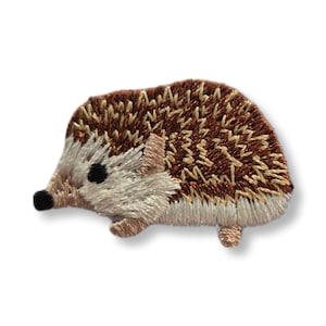 May include: Embroidered hedgehog patch featuring brown, tan, and cream colors. The patch has a detailed design with a textured appearance, showcasing the hedgehog's quills and body. The hedgehog has black eyes and a small nose.