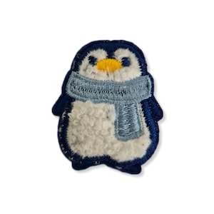 May include: A blue penguin with a white fluffy body wearing a light blue scarf. The penguin is embroidered and has a yellow beak.