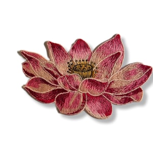 Puede incluir: Un parche bordado de flor de loto rosa con un centro amarillo. La flor está detallada con puntadas rosas y beige.