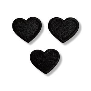 Pode incluir: Três patches pretos em forma de coração. Cada patch tem uma superfície texturizada e uma borda costurada. Os corações estão dispostos em um padrão triangular sobre um fundo branco. Adequado para artesanato têxtil.