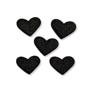 Puede incluir: Cinco parches de tela negros en forma de corazón sobre un fondo blanco. Los parches tienen un aspecto texturizado, y cada corazón tiene una orientación ligeramente diferente. Adecuado para varios proyectos de manualidades.