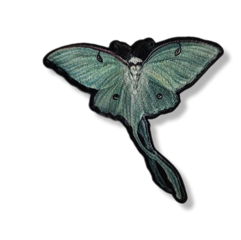 May include: Embroidered patch featuring a Luna moth design. The moth has light green wings with darker green and black details, and a black outline. The patch is likely for clothing or accessories.