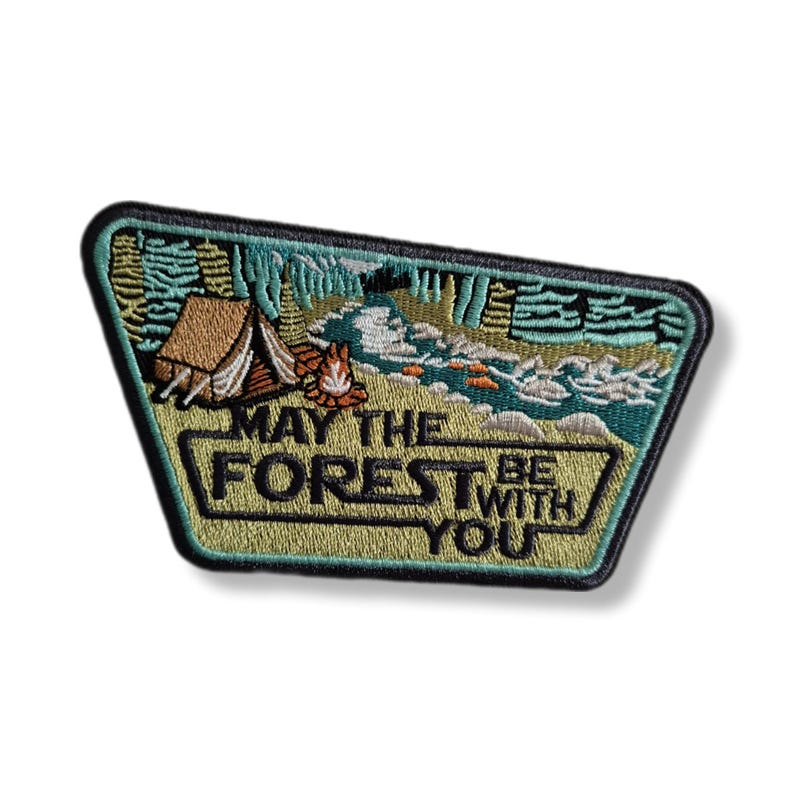 Peut inclure: &Eacute;cusson brod&eacute; avec une sc&egrave;ne de for&ecirc;t, comprenant une tente, un feu de camp et une rivi&egrave;re. L'&eacute;cusson a une bordure verte et le texte "MAY THE FOREST BE WITH YOU" en gras. L'&eacute;cusson est de forme rectangulaire avec des coins arrondis.