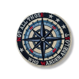 Peut inclure: Écusson brodé rond avec une rose des vents bleue marine et bleu clair, avec des accents rouges. Le patch porte l'inscription "NOT ALL THOSE WHO WANDER ARE LOST". Le patch a un fond crème.