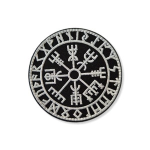 May include: A black and white embroidered patch featuring a compass with a circle of runes around the outside. The compass has four points with symbols and runes on each point.