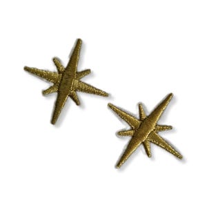 Puede incluir: Dos parches de planchado en forma de estrella dorada. Las estrellas tienen un diseño puntiagudo de seis puntas.