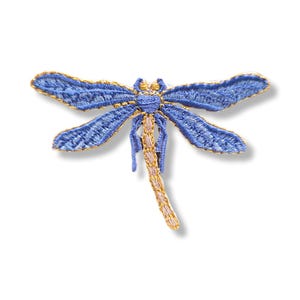 Peut inclure: Un écusson brodé en forme de libellule avec des ailes bleu vif bordées de fil doré. Le corps de l'insecte est segmenté avec des points de couture beige clair et dorés, créant une texture détaillée. Les ailes sont déployées symétriquement.