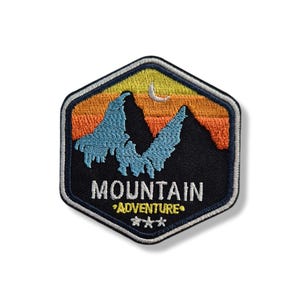 May include: Embroidered patch depicting a mountain scene. The patch has a black background with blue mountain peaks, an orange and yellow sunset, and a crescent moon. The text "MOUNTAIN ADVENTURE" is displayed.