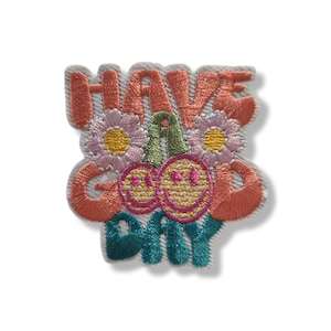 Puede incluir: Parche bordado con las palabras "HAVE A GOOD DAY" en coral, verde azulado y verde. El diseño incluye dos cerezas sonrientes y dos flores con pétalos rosas y centros amarillos. El parche tiene un borde blanco.
