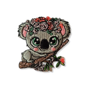May include: Embroidered iron-on patch of a gray koala bear wearing a pink and red flower crown, sitting on a brown branch with green leaves and pink flowers.
