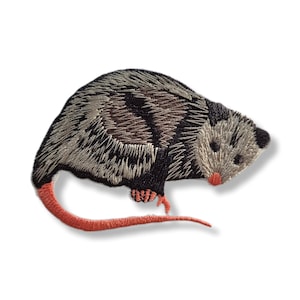 May include: Embroidered patch featuring an opossum. The opossum has gray and black fur with a pink nose, feet, and tail. The patch is designed to be ironed or sewn onto fabric, suitable for clothing or accessories.