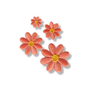 May include: A set of four embroidered flower patches in varying sizes. Each flower features coral-pink petals radiating from a circular, textured golden-yellow centre. The embroidery thread creates a visible, dense stitched pattern on each petal.