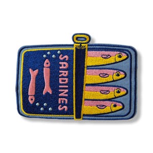 Könnte beinhalten: Gestickter Aufnäher mit einem Sardinendosen-Design. Der Aufnäher hat einen blauen Hintergrund mit dem Wort "SARDINES" in Gelb. In der Dose befinden sich vier rosa und gelbe Sardinen. Die Dose hat eine gelbe Lasche.