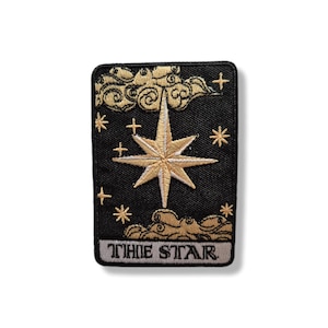 Könnte beinhalten: Schwarzer rechteckiger Aufnäher mit einem goldenen Stern, Wolken und anderen Himmelselementen. Der Aufnäher trägt die weißen Worte "THE STAR" am unteren Rand. Der Stern ist das zentrale Element, mit acht Spitzen und einem goldenen Umriss.
