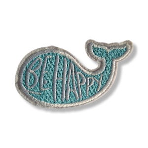 以下が含まれることがあります： 「BE HAPPY」の文字が白で刺繍された、ターコイズ色のクジラ型のパッチ。パッチは灰色の縁取りがあり、生地にアイロンをかけたり縫い付けたりするように設計されています。クジラのデザインは陽気でポジティブなイメージです。