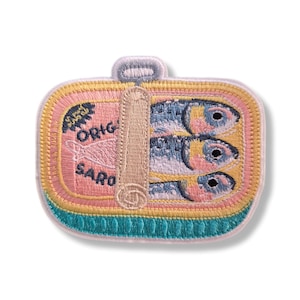 Pode incluir: Um emblema bordado retangular apresentando uma lata de sardinhas rosa com três peixes azuis e amarelos dentro. O design inclui uma chave de abertura de metal bege no topo e o texto ORIG e SARO em azul escuro sobre o fundo rosa.