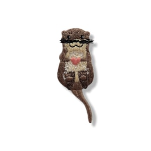 Peut inclure: Écusson brodé représentant une loutre de dessin animé avec une moustache noire et un cœur rose. La loutre a une fourrure brune avec des détails beiges et blancs. Le patch est conçu pour être repassé ou cousu sur du tissu.