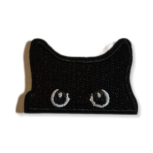 Peut inclure: Écusson de visage de chat brodé noir avec des yeux blancs. Le patch présente un design simple et stylisé d'un visage de chat, parfait pour ajouter à des vêtements ou des accessoires. Les yeux du chat sont détaillés avec du fil blanc.