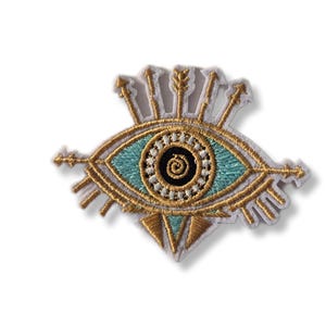 Peut inclure: Écusson brodé représentant un œil avec des accents dorés et turquoise. L'œil a un iris turquoise, une pupille noire et des détails dorés. Des flèches et des triangles dorés entourent l'œil, sur fond blanc. Parfait pour vêtements ou accessoires.