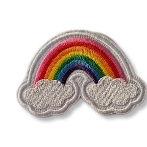Peut inclure: Un patch brodé en forme d'arc-en-ciel avec des couleurs rose, rouge, orange, jaune, vert, bleu, indigo et violet. L'arc-en-ciel est arqué au-dessus de deux nuages blancs.