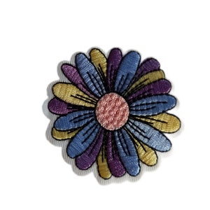 Peut inclure: Un patch brodé de fleur coloré avec des pétales bleus, violets, jaunes et roses. La fleur est soulignée de noir.