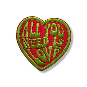 Peut inclure: Écusson brodé en forme de cœur rouge avec des bordures vertes. Le texte "ALL YOU NEED IS LOVE" est brodé en vert sur le cœur. Un accessoire décoratif pour vêtements.