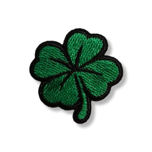Peut inclure: Un écusson vert en forme de trèfle à quatre feuilles avec un contour noir. Le trèfle est brodé avec un aspect texturé, et le motif est centré sur un fond blanc. Ce patch est un symbole de chance, souvent associé à la Saint-Patrick.
