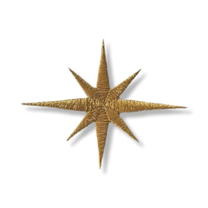 May include: A gold-colored, eight-pointed star with a textured, woven appearance. The star has sharp, elongated points radiating from a central hub. The star is set against a white background, casting a subtle shadow.