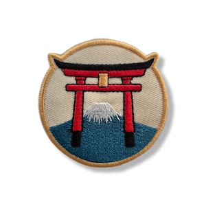 Op de afbeelding: Geborduurde patch met een rode Torii-poort, een witte berg en blauw water, tegen een beige achtergrond. De patch heeft een gouden rand en is cirkelvormig. Het ontwerp roept Japanse beelden op.