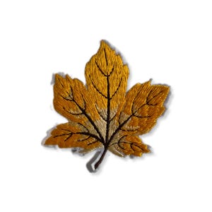 Op de afbeelding: Een gele geborduurde esdoornblaadjespatch. Het blad is gedetailleerd met bruine nerven en een bruine steel.